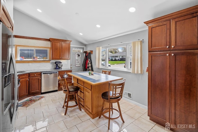 kitchen featuring dishwasher, lofted ceiling, a breakfast bar area, light tile patterned flooring, and a kitchen island