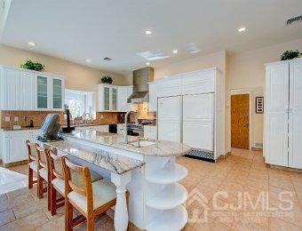 kitchen with light stone countertops, a kitchen island with sink, wall chimney exhaust hood, and white cabinetry