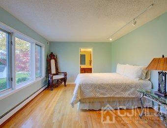 bedroom with rail lighting, light wood-type flooring, a textured ceiling, ensuite bathroom, and a baseboard radiator