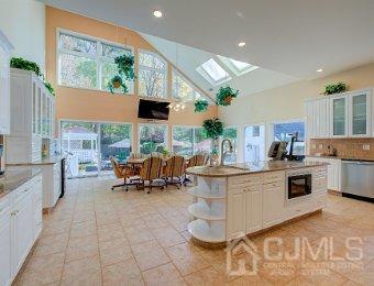 kitchen with white cabinetry, black microwave, tasteful backsplash, a skylight, and a center island with sink