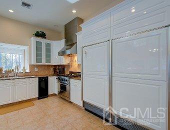 kitchen with wall chimney range hood, decorative backsplash, white cabinetry, high end stove, and sink