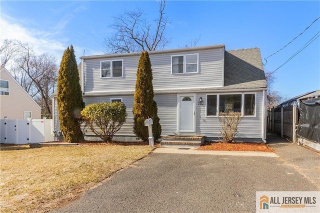 view of front of home with a shingled roof, a front lawn, fence, and a gate