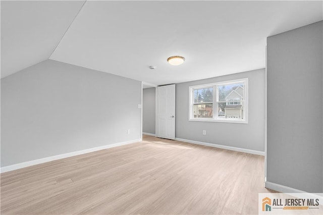 interior space featuring light wood-style flooring, baseboards, and vaulted ceiling