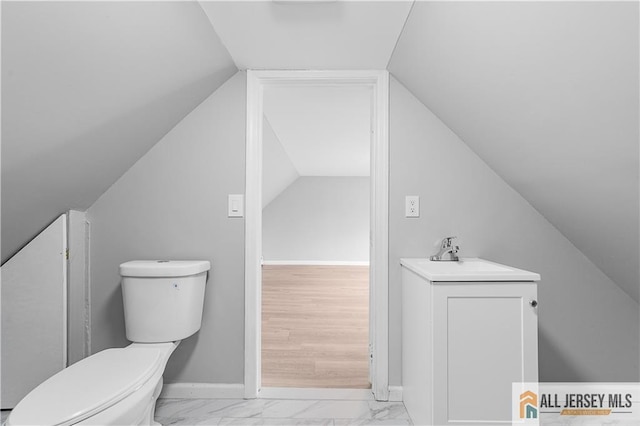 bathroom featuring toilet, marble finish floor, a sink, lofted ceiling, and baseboards