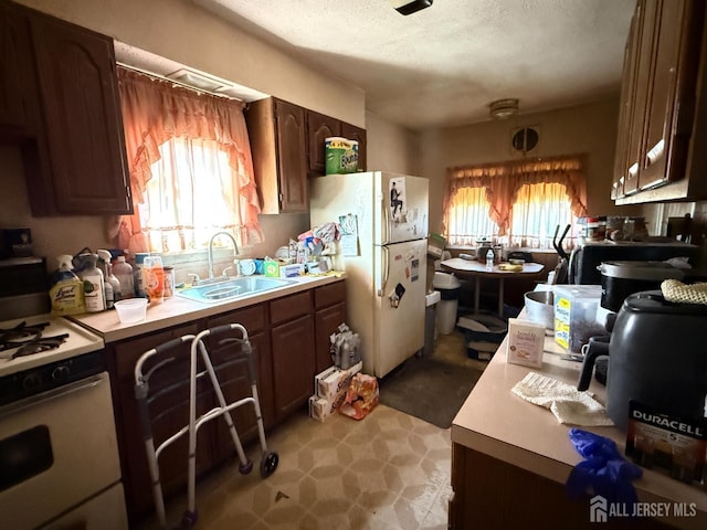 kitchen with a sink, light countertops, white appliances, a textured ceiling, and light floors