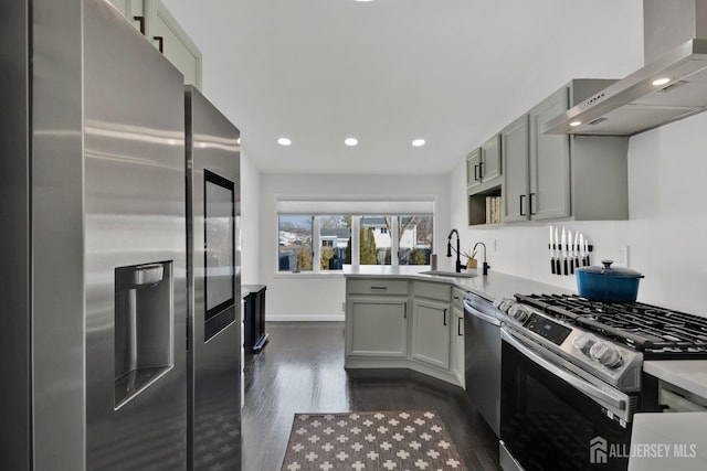 kitchen featuring light countertops, appliances with stainless steel finishes, a sink, wall chimney range hood, and a peninsula