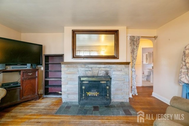 living area with wood finished floors, baseboards, and a stone fireplace