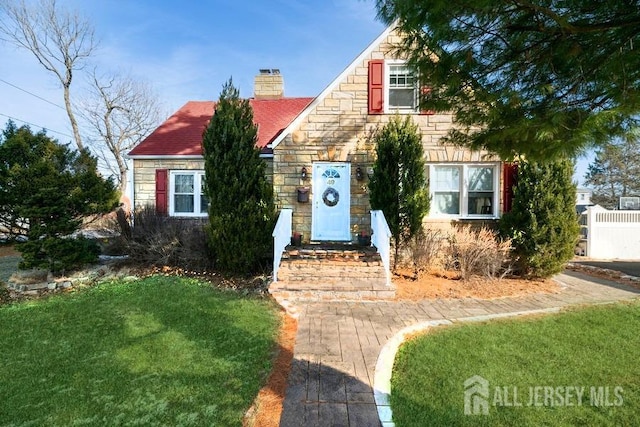 view of front of home with stone siding, a chimney, fence, and a front yard