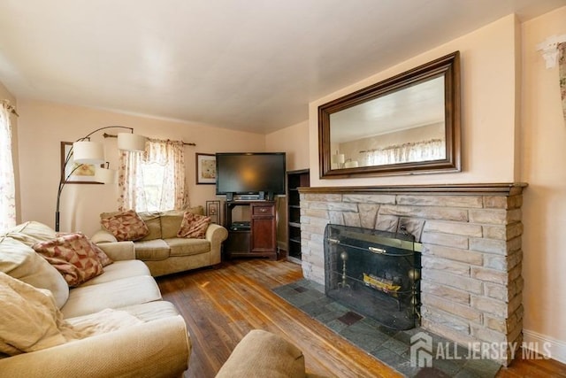 living room with dark wood-style flooring and a stone fireplace