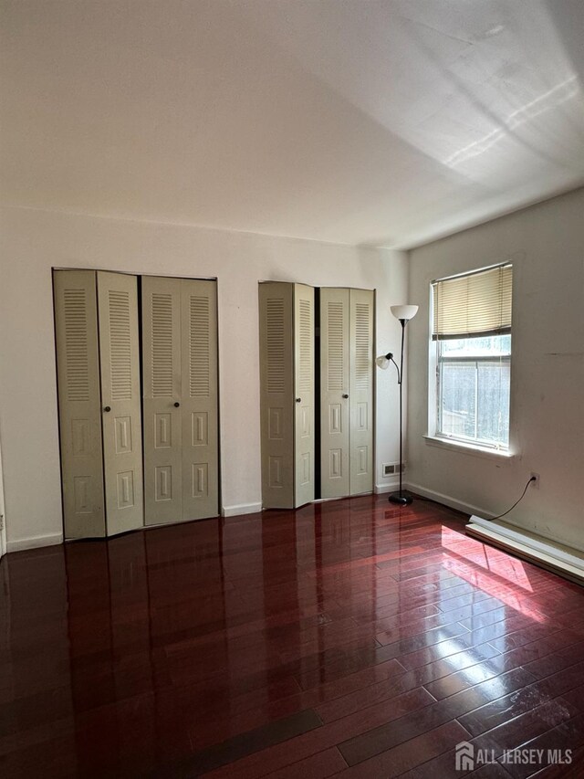 unfurnished bedroom with dark wood-type flooring and two closets