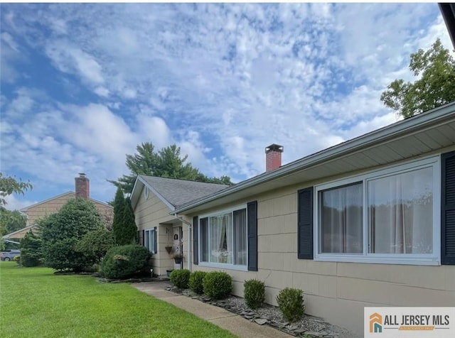 view of side of home with a chimney and a lawn