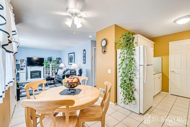 dining space featuring ceiling fan, light tile patterned flooring, a fireplace, and visible vents