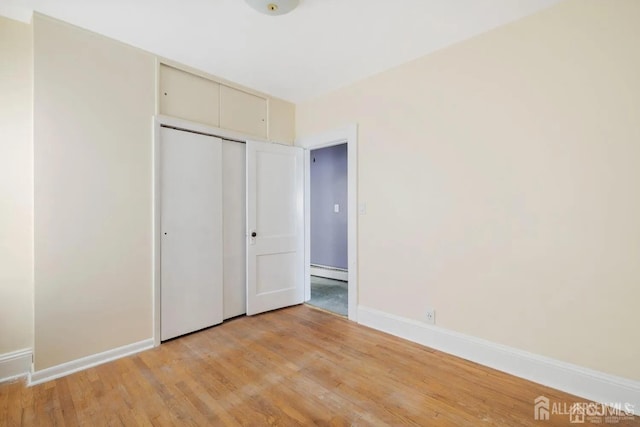 unfurnished bedroom with a closet, light wood-style flooring, a baseboard heating unit, and baseboards