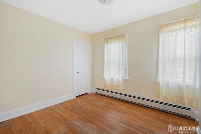 empty room with hardwood / wood-style floors, baseboard heating, and baseboards