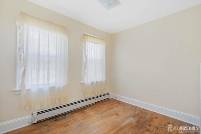 unfurnished room featuring wood finished floors, a baseboard heating unit, and baseboards