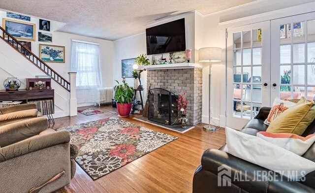 living room featuring french doors, a brick fireplace, a textured ceiling, radiator, and hardwood / wood-style flooring