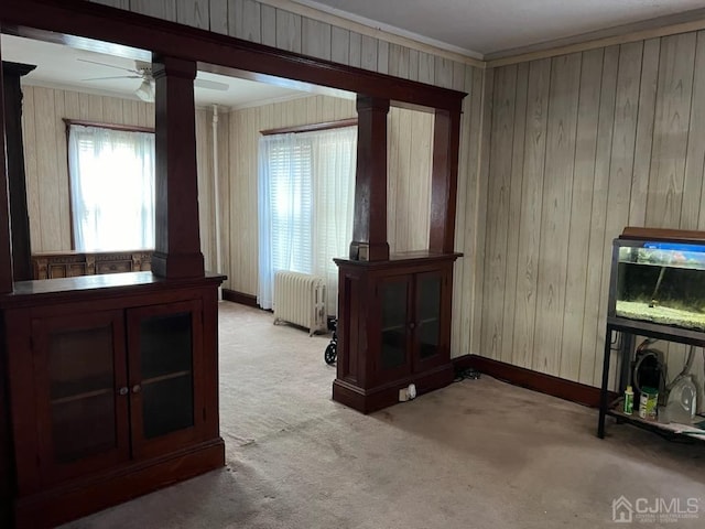 interior space featuring ornamental molding, light colored carpet, ceiling fan, wooden walls, and radiator heating unit