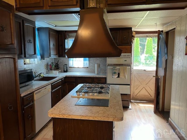 kitchen with sink, stainless steel appliances, tasteful backsplash, range hood, and a kitchen island