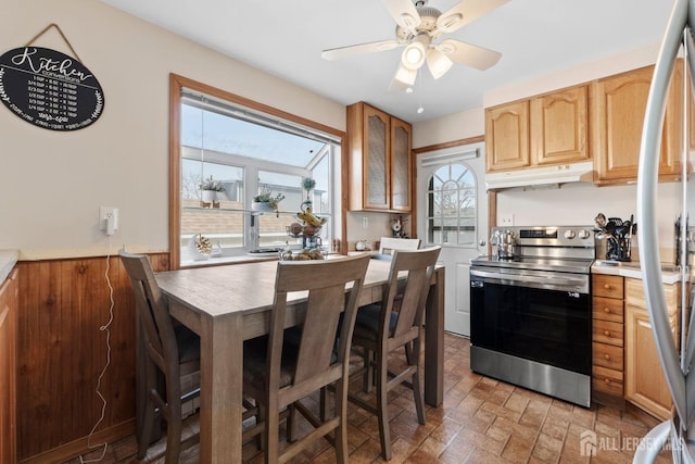 kitchen featuring stainless steel electric range oven, light brown cabinetry, ceiling fan, wainscoting, and under cabinet range hood