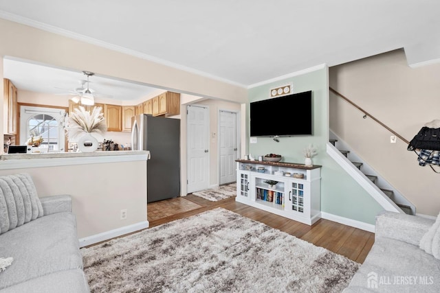 living room featuring crown molding, a ceiling fan, baseboards, wood finished floors, and stairway