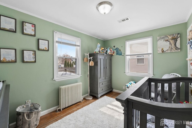 bedroom with radiator heating unit, ornamental molding, wood finished floors, and visible vents