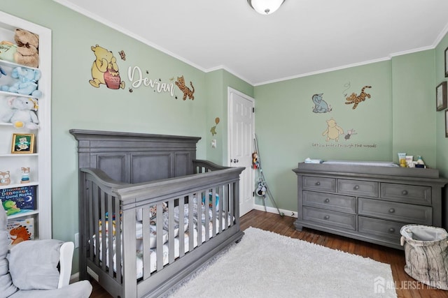 bedroom featuring baseboards, ornamental molding, a crib, and dark wood-style floors