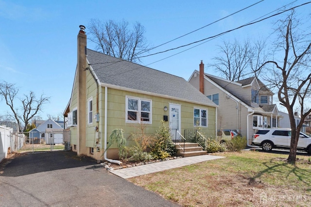 view of front of home featuring a front lawn, roof with shingles, fence, and a chimney