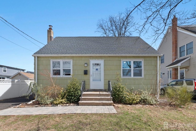 view of front of home featuring roof with shingles, fence, a front yard, and a chimney
