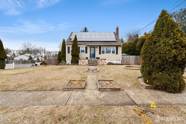 view of front of home with a chimney, a front yard, fence, and roof mounted solar panels