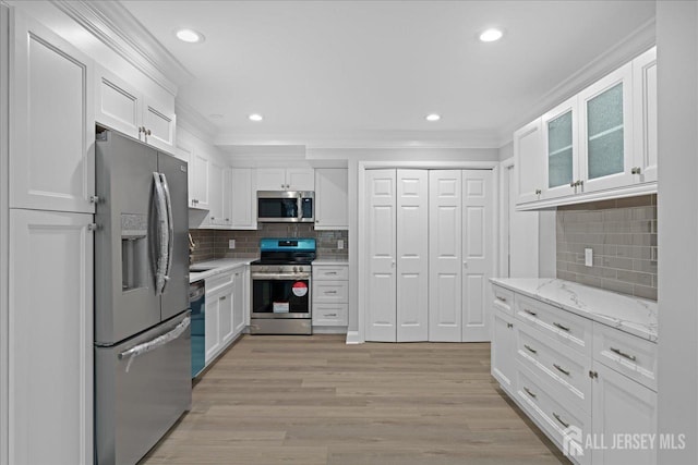 kitchen featuring white cabinets, light stone countertops, stainless steel appliances, and ornamental molding