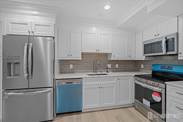 kitchen with appliances with stainless steel finishes, light wood-type flooring, white cabinets, crown molding, and sink