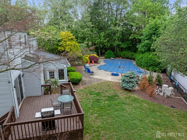 view of grassy yard featuring a deck, a covered pool, a patio area, outdoor dining area, and view of scattered trees