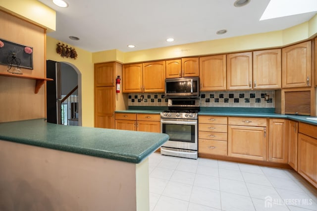 kitchen featuring backsplash, arched walkways, light tile patterned floors, dark countertops, and appliances with stainless steel finishes