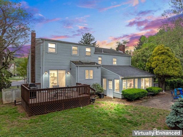 back of property at dusk featuring fence, a deck, a chimney, and a lawn
