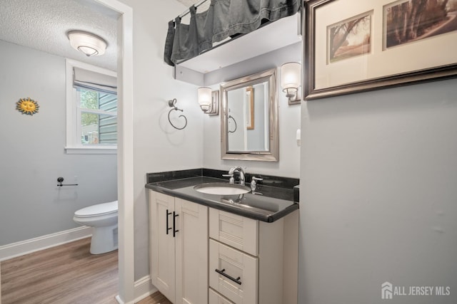 bathroom featuring toilet, wood finished floors, vanity, a textured ceiling, and baseboards