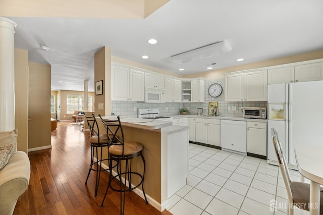 44 Windsong Cir E, Brunswick, NJ 08816 - kitchen featuring white appliances, ornate columns, a breakfast bar, a peninsula, and backsplash