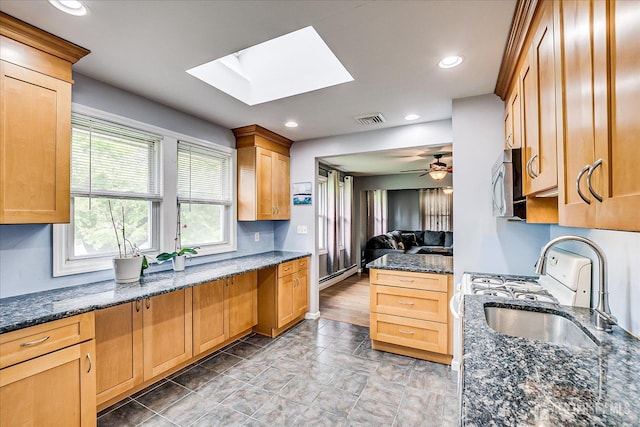 kitchen with a skylight, open floor plan, dark stone counters, stainless steel microwave, and recessed lighting