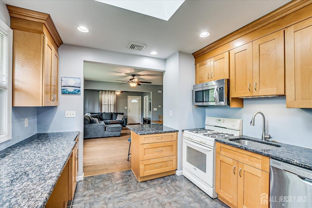kitchen featuring appliances with stainless steel finishes, a sink, open floor plan, dark stone countertops, and a ceiling fan