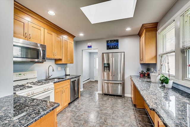 kitchen featuring appliances with stainless steel finishes, a sink, a baseboard radiator, dark stone countertops, and a skylight