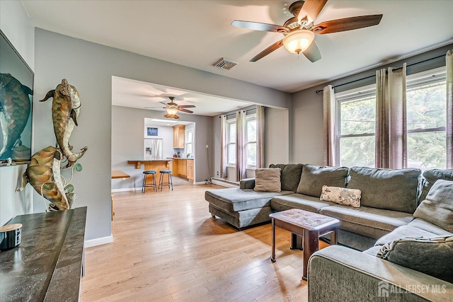 living room with a ceiling fan, light wood-style flooring, a baseboard heating unit, and baseboards