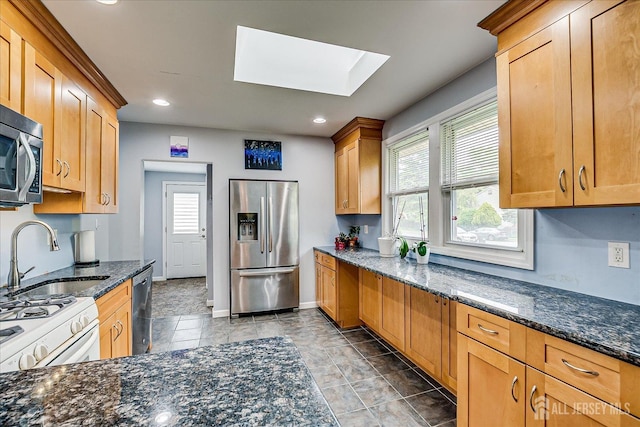 kitchen featuring appliances with stainless steel finishes, a sink, a skylight, dark stone counters, and recessed lighting