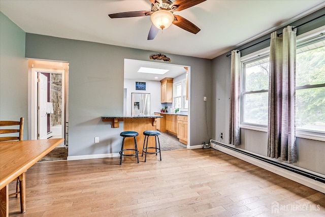 kitchen featuring stainless steel fridge, a baseboard heating unit, a kitchen bar, light wood-style floors, and light brown cabinetry