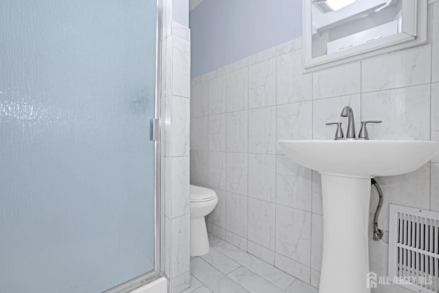 bathroom featuring toilet, visible vents, tile walls, marble finish floor, and a shower stall