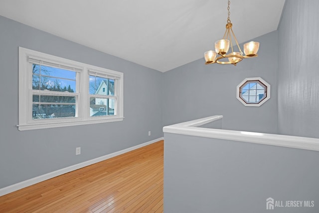 spare room featuring lofted ceiling, hardwood / wood-style flooring, baseboards, and a chandelier