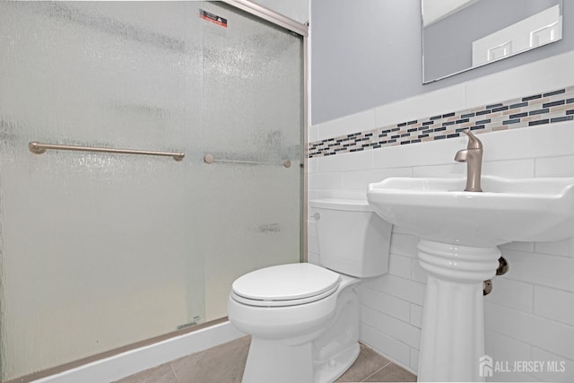 bathroom featuring toilet, a stall shower, tile patterned flooring, and tile walls