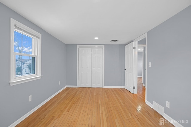 unfurnished bedroom with light wood finished floors, a closet, visible vents, and baseboards