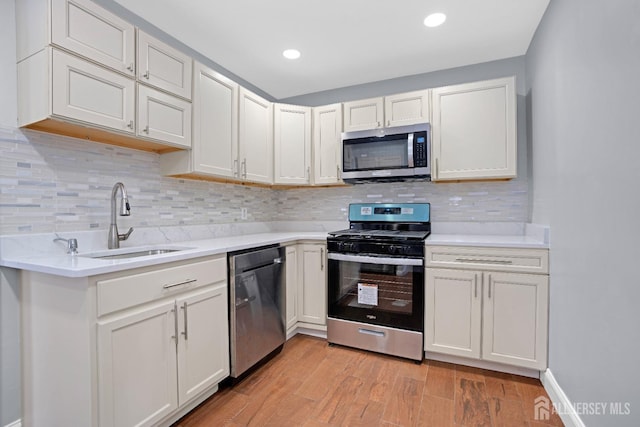 kitchen with light wood-style flooring, a sink, stainless steel appliances, light countertops, and backsplash