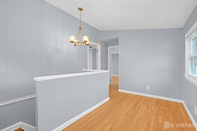 spare room featuring baseboards, hardwood / wood-style floors, and an inviting chandelier