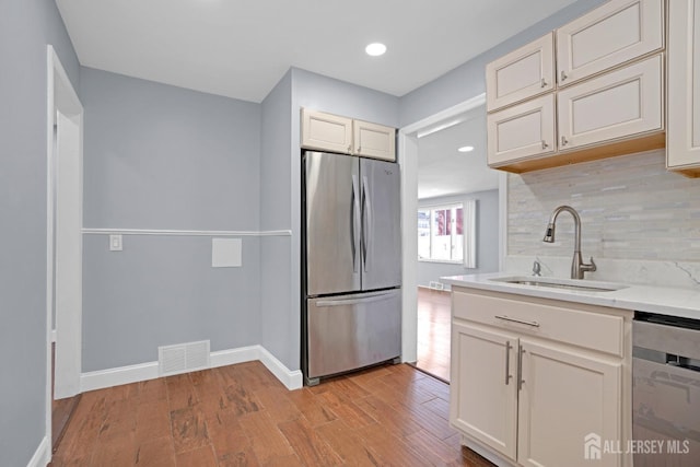 kitchen featuring light wood-style flooring, stainless steel appliances, a sink, light countertops, and tasteful backsplash