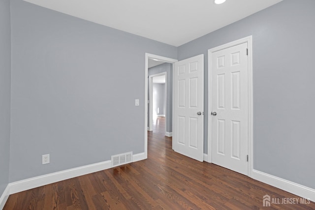 unfurnished bedroom with dark wood-type flooring, visible vents, and baseboards